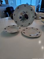 Three plates showing the scalloped edge, floral center pattern, and smaller leaf motifs around the edge.