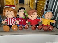 Front view of the four plush talking Peanuts characters seated side by side: Peppermint Patty, Lucy Van Pelt, Charlie Brown, Linus with shepherd's staff.
