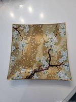 Top view of square plate showing detailed cherry blossom design on gold background