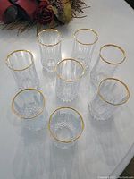 Top-down and angled view of all eight lead crystal tumblers arranged in a circle showing gold rims and cut crystal design.