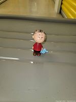 Front side view of Linus figurine wearing a red shirt holding blue blanket.