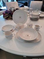 Photo showing an arrangement of the dinnerware set including plates, bowls, cups, creamer, sugar container, and serving dishes on a white table.