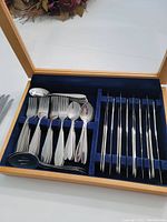Open wooden holder showing forks, spoons, and knives arranged in blue velvet slots.