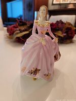 Front view of figurine showing the detailed pink dress with gold rose accents and ruffled neckline.