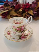 Bone china tea cup on matching saucer with pink rose design and gold trim, 'June' inscribed inside the cup