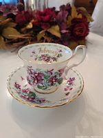 Front angled view of February Royal Albert tea cup on matching saucer with violet floral design and gold trim.