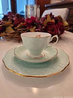 Teacup placed on matching saucer, atop coordinating plate, showing scales and overall design detail including polka dots and gold trim.