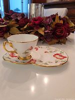 Side view of Royal Albert 1970's Poppy teacup placed on matching tennis saucer surrounded by floral decoration, showing gold trim and red poppy pattern.