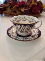 Side view of the teacup sitting on the saucer, showing detailed decorative pattern with floral and gold filigree on white and blue background.