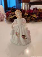 Front-side view of the porcelain figurine showing the young girl with pink roses on her white dress and pink puffed sleeves.