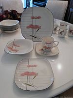 Multiple pastel pink flower square plates, cups, saucers arranged on white table showcasing pattern and shape.