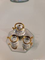 Three-piece Swarovski tea set with a crystal teapot and two teacups, showing gold-plated details on rims and handles, placed on a mirror base.