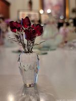 Crystal red rose flower arrangement in faceted clear crystal vase with silver-tone rhodium stems and leaves, photographed on table with blurred background.