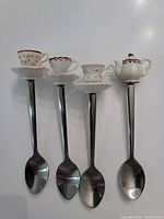 Four metal spoons with ceramic miniature tea cups on handles in pastel colors and gold rims