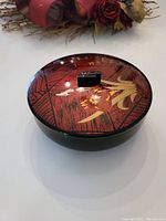 Top view of the vintage Japanese lacquered bowl showing the gold cherry blossom flower decoration on the lid with textured reddish background and small black handle.