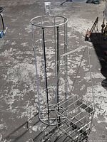 Metal recreational ball holder and metal tennis ball collector basket on concrete floor outdoors.