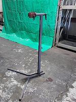 Full view of standing bike repair rack showing vertical post, clamp, and base on industrial floor.