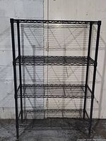 Full view of the black metal wire shelving unit with four shelves and adjustable feet.