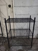 Front view of black metal 3-tier wire storage shelf showing all three shelves and vertical supports.