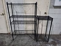 Front view of two black metal wire storage shelves placed side by side against a white wall with closed doors, showing overall structure and size difference.
