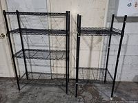 Two black metal wire shelving units each with three shelves side by side against a wall.