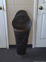 Full view of tall brass umbrella stand showing front embossed details and overall shape.