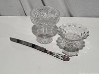 Photo showing two clear glass candy dishes and an enamel handle dessert cutting tool on a white surface, angled view.