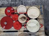 Top-down view of red cast enamel cookware set showing pots, pans, lids, and a ladle arranged on a pallet surface.