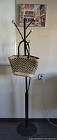 Black metal coat rack with a woven tote bag hanging on it, wall picture above