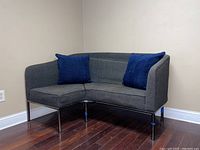 Gray fabric contemporary corner couch with two blue accent pillows, set against a neutral background.