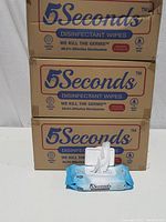 Three cardboard boxes labeled '5Seconds Disinfectant Wipes' stacked, with one pack of wipes in front showing packaging design and branding.