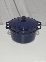 Blue cast enamel Dutch oven with double handles. Shown outdoors on table against white background.