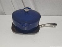 Blue enamel Dutch oven with lid placed on top of a square griddle skillet with metal handle on white surface.