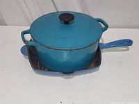 Blue enamel Dutch oven with lid sitting inside a square blue enamel griddle skillet, both showing rust and wear.