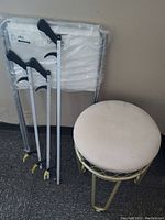 Three reach grabbers, folding laundry bag on stand, and round stool arranged side by side against wall on floor
