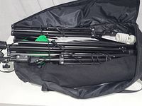 Overview photo showing black metal stands, green fabric backdrop, and lighting bulbs packed inside a black carrying bag.