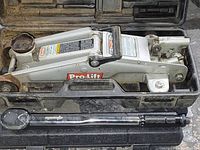 View of Pro-Lift hydraulic floor jack and Epauto torque wrench in the case on concrete floor, tools dusty and showing signs of use.