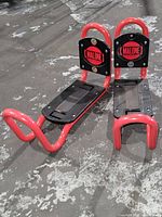 Pair of Malone kayak racks shown from side angle on concrete surface, showing red tubular metal frames and black padded cradle components with Malone branding.