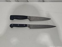 Two Zwilling J.A. Henckels knives laid side by side showing blades and handles on white surface.