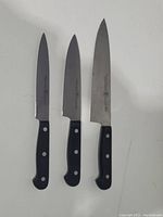 Three Zwilling J.A. Henckels kitchen knives with black handles, showing front side of blades and logos.