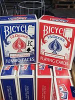 Two large boxes of Bicycle playing cards, one Amazon style Jumbo Faces with mix of red and blue decks and one regular Casino style box of 13 decks in red and blue, both labeled with price sticker.