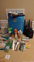 Full lot view showing large blue waterproof box, thermoses, water container, bug repellants, utensils, fishing jigs, solar shower and other camping accessories.