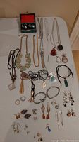 Wide view of assorted costume jewelry items arranged on a beige surface including necklaces, rings, bracelets, and earrings.