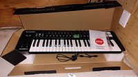 M-Audio Oxygen 49 electric keyboard in open box with power cord and packaging material visible.