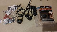 Lot comprising two used Garmin BarkLimiter dog collar devices with adjustable dials, various metal accessories, instruction sheets, and one new Garmin BarkLimiter replacement collar sealed in original packaging.