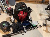 Photo of full ski gear lot arranged on floor with boots, gloves, helmet, backpack, ski poles, toques, and headband.