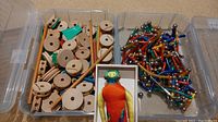 Photo of wooden Tinker Toys pieces on left, Magnetix magnetic rods and spheres on right, and multicolored fabric doll in center inside plastic storage boxes.