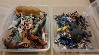 Two plastic bins filled with various dinosaur and prehistoric animal action figures, viewed from above
