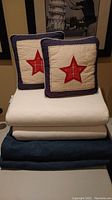 Stack of bedding and pillows showing two denim duvet covers (dark blue), atop several white foam pillows, and two Pottery Barn Kids square throw pillows with red star applique on top