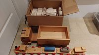 Overall view of wooden truck with box bed and adjacent box containing wooden blocks; a wooden train set visible in front.